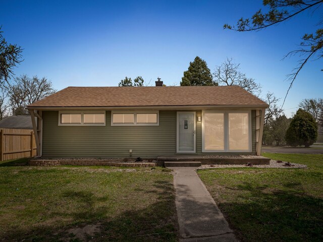 view of front of property featuring fence, a chimney, roof with shingles, and a front yard