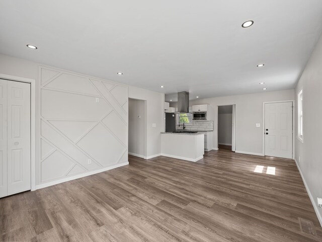 unfurnished living room with a sink, baseboards, recessed lighting, and wood finished floors