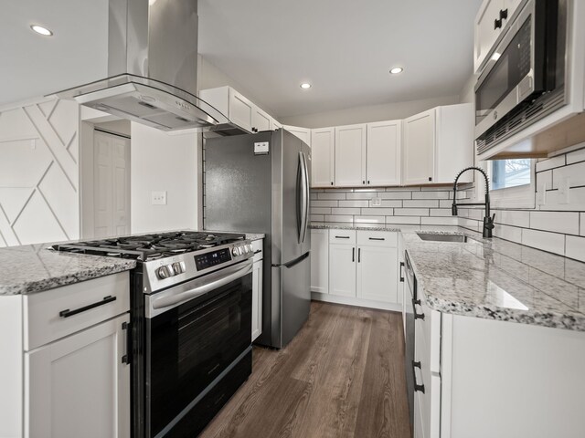kitchen with white cabinets, appliances with stainless steel finishes, a sink, island range hood, and backsplash