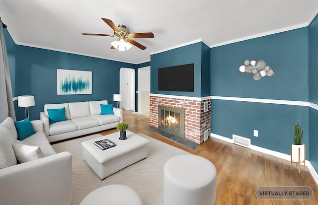 living area with a ceiling fan, wood finished floors, baseboards, a fireplace, and crown molding