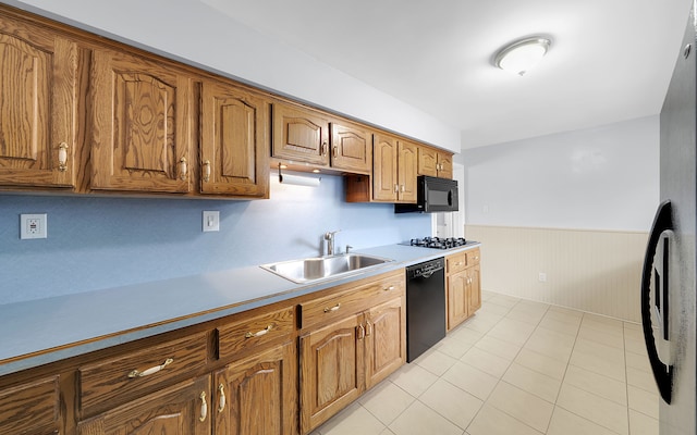 kitchen featuring black appliances, a sink, wainscoting, brown cabinetry, and light countertops