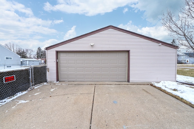 snow covered garage featuring a detached garage and fence
