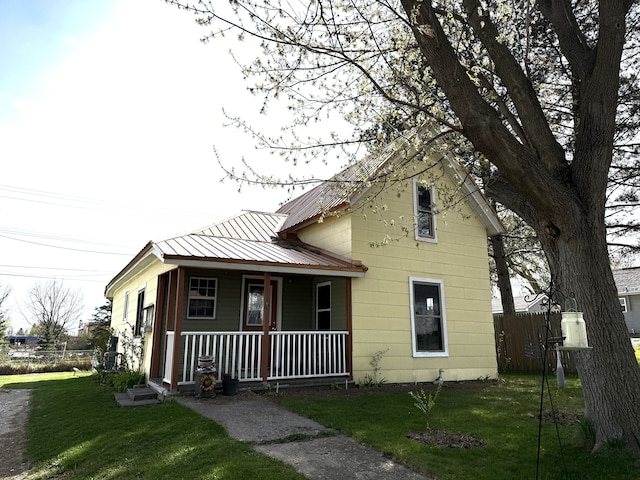 view of front facade featuring fence, covered porch, metal roof, and a front yard