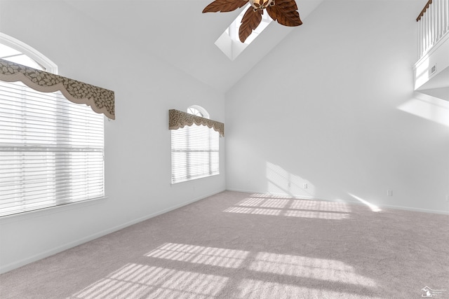 carpeted spare room with baseboards, ceiling fan, a skylight, and high vaulted ceiling
