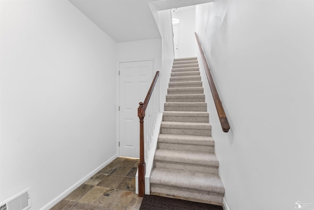 stairway with visible vents, baseboards, and stone finish floor