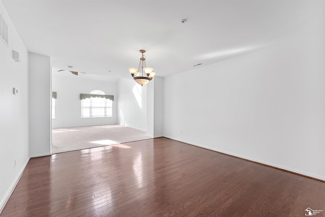 spare room with visible vents, baseboards, wood finished floors, and a chandelier