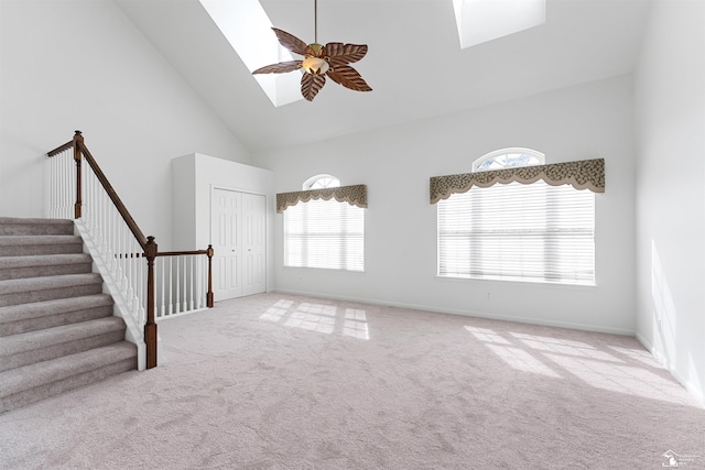 unfurnished living room with stairway, a skylight, carpet, and high vaulted ceiling