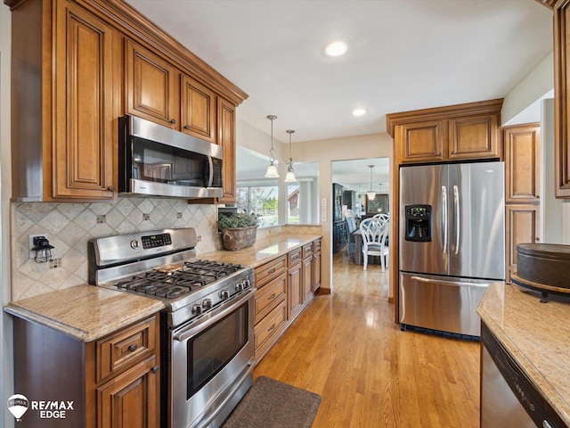 kitchen featuring appliances with stainless steel finishes, light wood-style floors, brown cabinetry, decorative light fixtures, and decorative backsplash