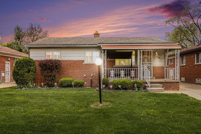 bungalow-style home with brick siding, a front lawn, a chimney, and covered porch