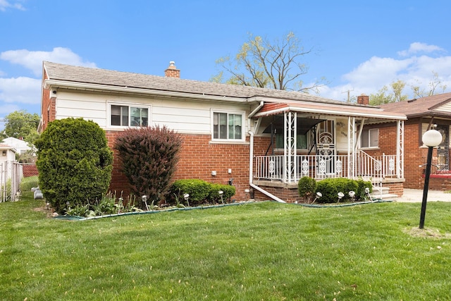 view of front of house with a chimney, a front yard, brick siding, and a porch