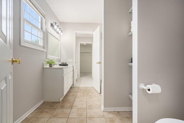 bathroom featuring baseboards, a walk in closet, tile patterned flooring, and vanity