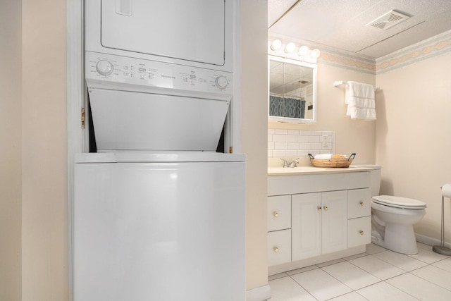 bathroom featuring visible vents, vanity, stacked washer / dryer, toilet, and backsplash