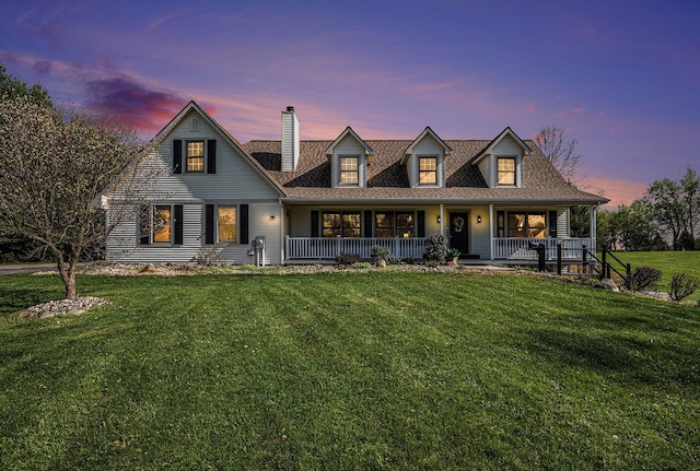 cape cod-style house with a lawn, a shingled roof, covered porch, and a chimney