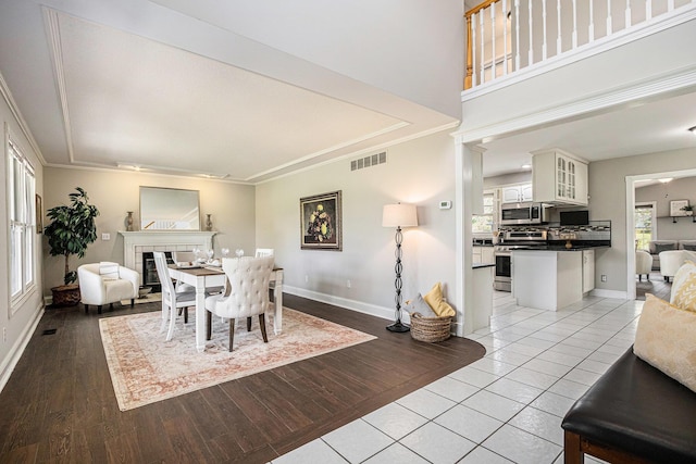 dining space with visible vents, crown molding, baseboards, a tiled fireplace, and light tile patterned floors