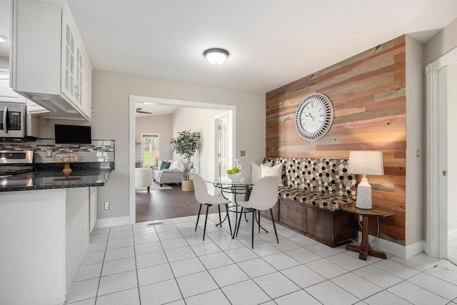 dining area with baseboards, wood walls, an accent wall, and light tile patterned flooring