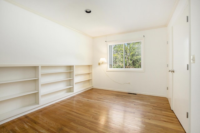 unfurnished room featuring light wood-style floors, baseboards, crown molding, and visible vents