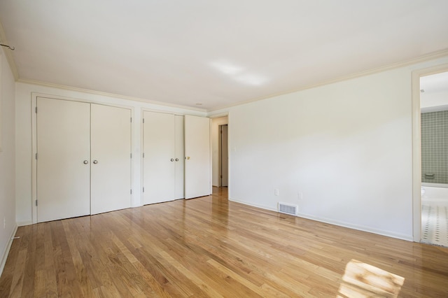 unfurnished bedroom with ornamental molding, two closets, light wood finished floors, and visible vents