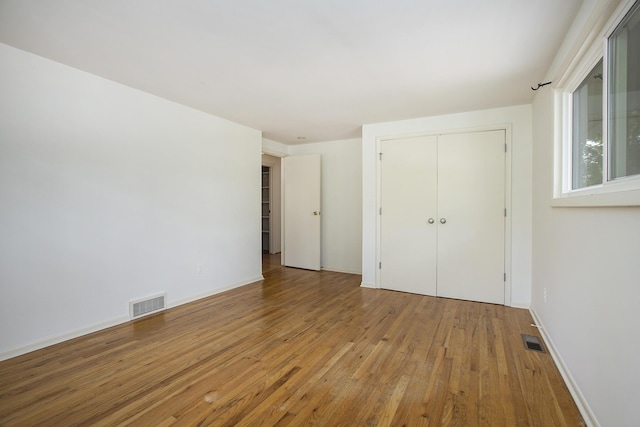unfurnished bedroom with visible vents, wood-type flooring, and a closet