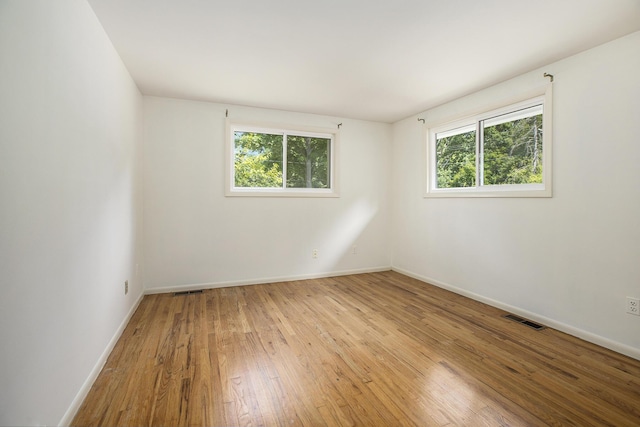 unfurnished room featuring visible vents, wood-type flooring, baseboards, and a healthy amount of sunlight
