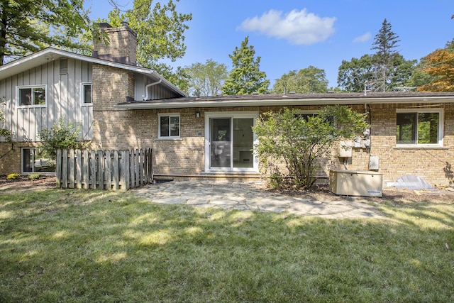 rear view of house featuring board and batten siding, a chimney, a lawn, a patio area, and brick siding
