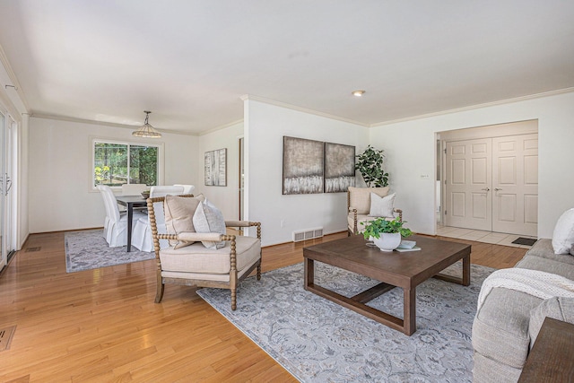 living area featuring visible vents, ornamental molding, and light wood-type flooring