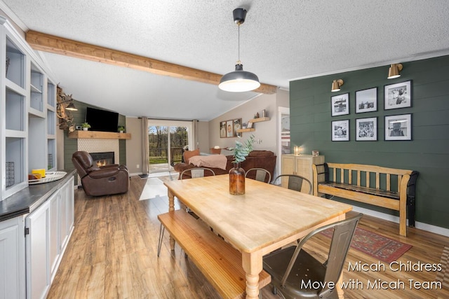 dining space with vaulted ceiling with beams, light wood finished floors, baseboards, and a fireplace