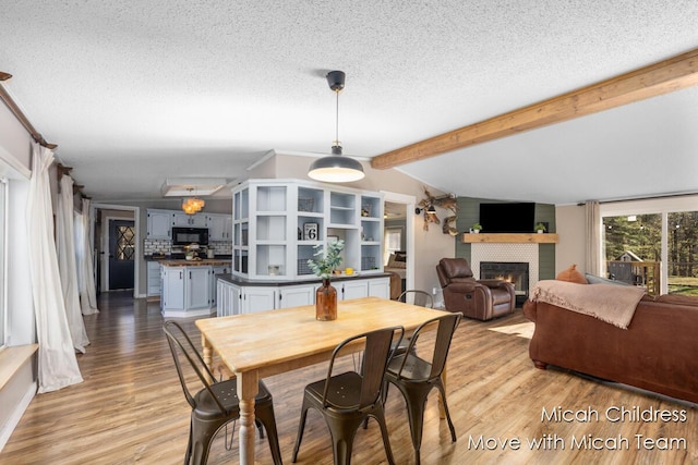 dining room featuring vaulted ceiling with beams, a textured ceiling, a fireplace, and light wood-type flooring