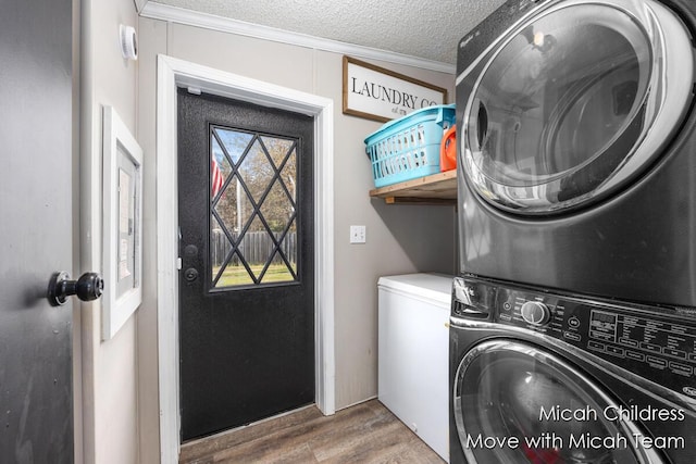 washroom with stacked washer / drying machine, laundry area, a textured ceiling, wood finished floors, and ornamental molding
