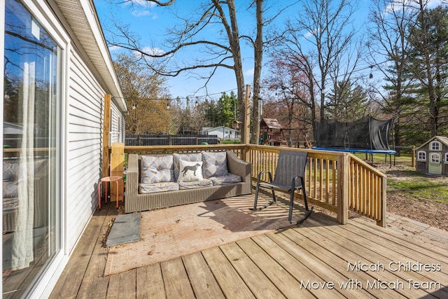 deck with outdoor lounge area, fence, a shed, a trampoline, and an outbuilding