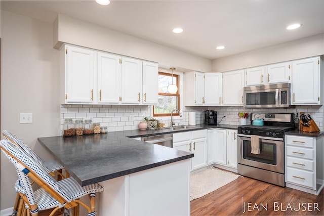 kitchen featuring dark countertops, a sink, white cabinets, a peninsula, and stainless steel appliances