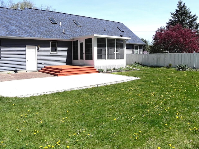 rear view of house featuring roof with shingles, fence, a sunroom, and a patio area