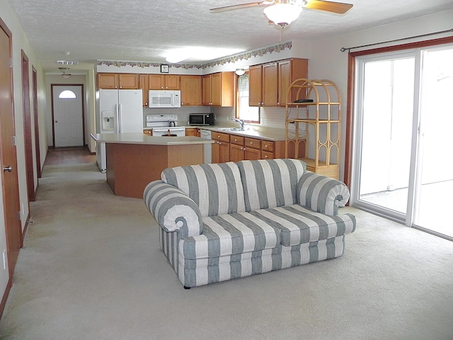 kitchen with brown cabinets, light carpet, a sink, white appliances, and a kitchen island