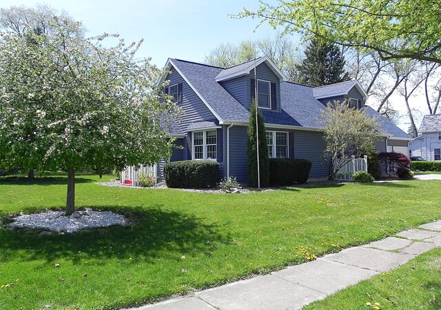 view of front facade with a shingled roof and a front yard