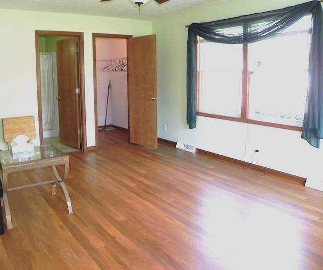 unfurnished bedroom featuring baseboards, a walk in closet, visible vents, and wood finished floors