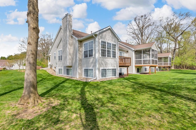 rear view of property with a yard, a chimney, a sunroom, and a wooden deck