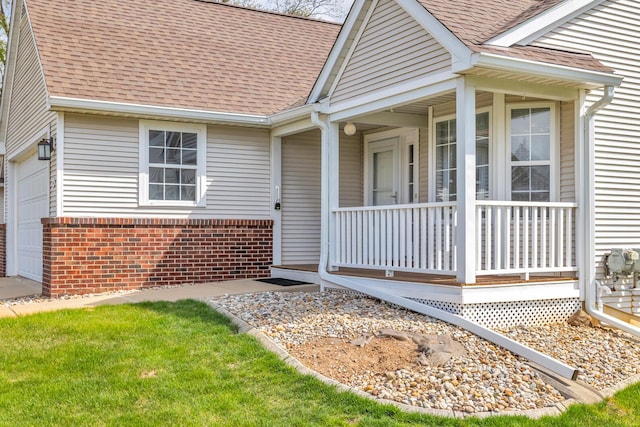 view of exterior entry with brick siding, a shingled roof, an attached garage, and covered porch