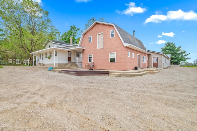 exterior space featuring a porch, a gambrel roof, driveway, and brick siding