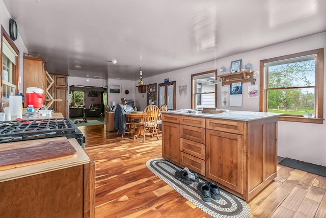 kitchen with a center island, brown cabinets, light wood-type flooring, light countertops, and black gas range oven