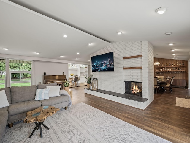 living room with vaulted ceiling with beams, a brick fireplace, and wood finished floors