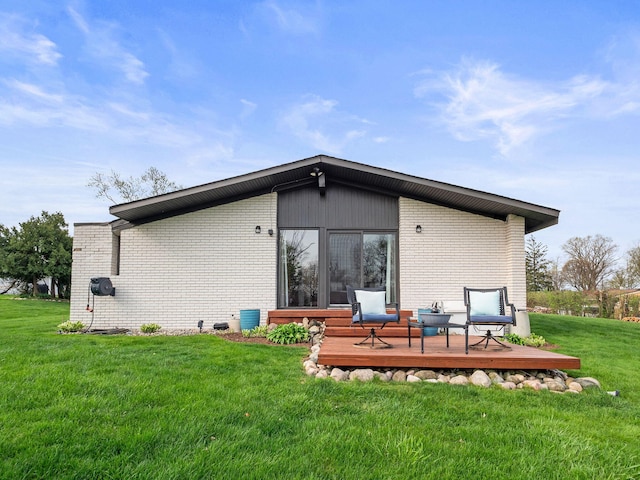 rear view of property featuring brick siding, a lawn, and a wooden deck