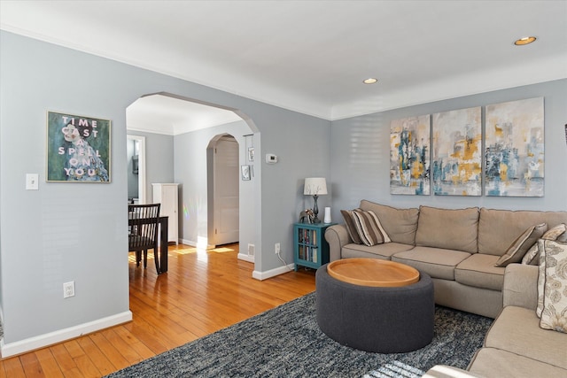 living area with arched walkways, baseboards, and light wood-style flooring