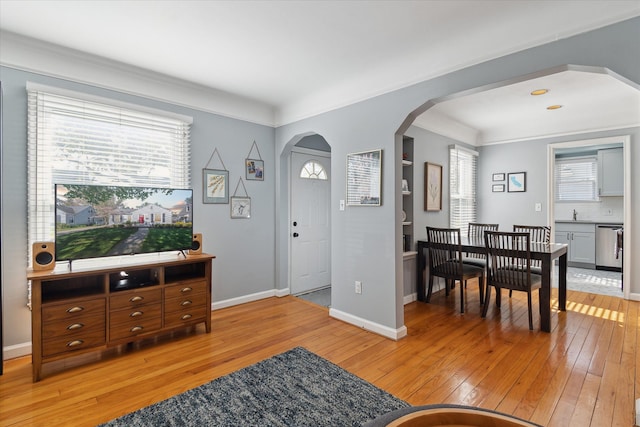 interior space featuring crown molding, arched walkways, baseboards, and light wood finished floors