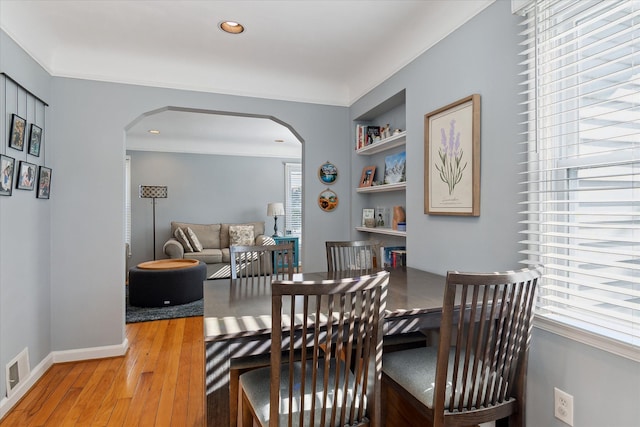 dining area with arched walkways, built in shelves, a wealth of natural light, and hardwood / wood-style floors
