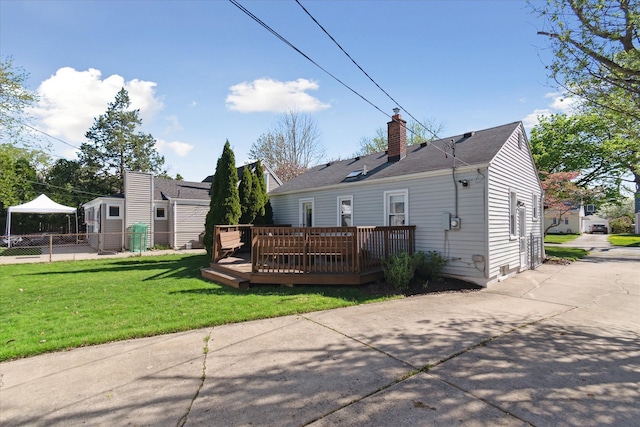 back of house with a chimney, a deck, fence, a yard, and a shingled roof