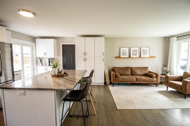 kitchen with light stone countertops, freestanding refrigerator, white cabinetry, a kitchen bar, and a kitchen island