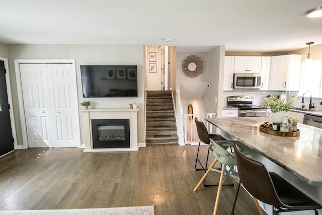 kitchen featuring light stone countertops, appliances with stainless steel finishes, a sink, a kitchen breakfast bar, and white cabinetry