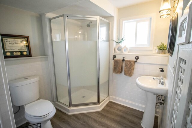 bathroom with toilet, tile walls, a shower stall, and wood finished floors