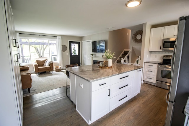 kitchen featuring a kitchen island, open floor plan, appliances with stainless steel finishes, and dark wood-type flooring