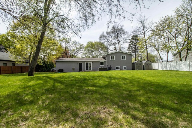 rear view of house with a storage unit, a lawn, fence, and an outbuilding