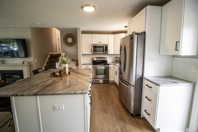 kitchen with dark wood-style flooring, stainless steel appliances, light stone counters, and decorative backsplash